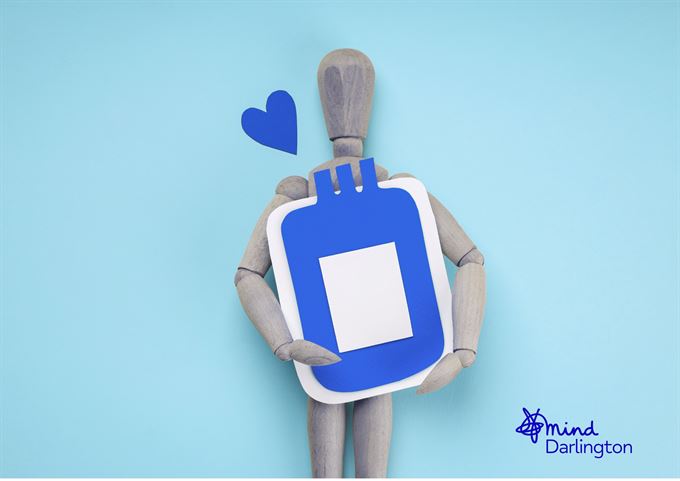 Photograph of a wooden mannequin holding a blue and white hot water bottle against a light blue background, with a small blue heart shape near its head.